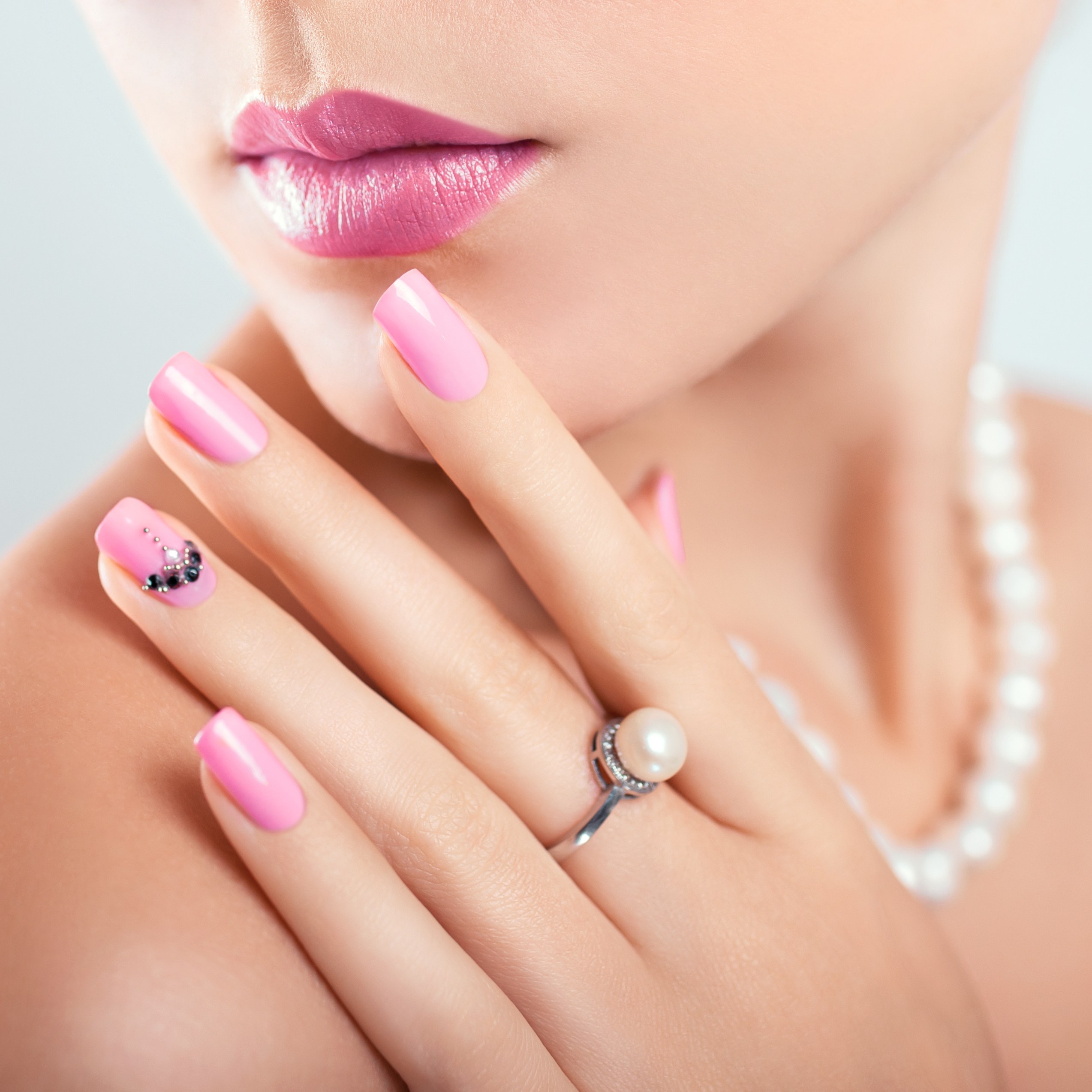 Frau mit Perlenschmuck zeigt eine rosa Maniküre